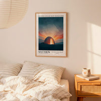 a poster of a sunset with a message about Matthew, a biblical figure, hanging on a wall above a bed with striped bedding.