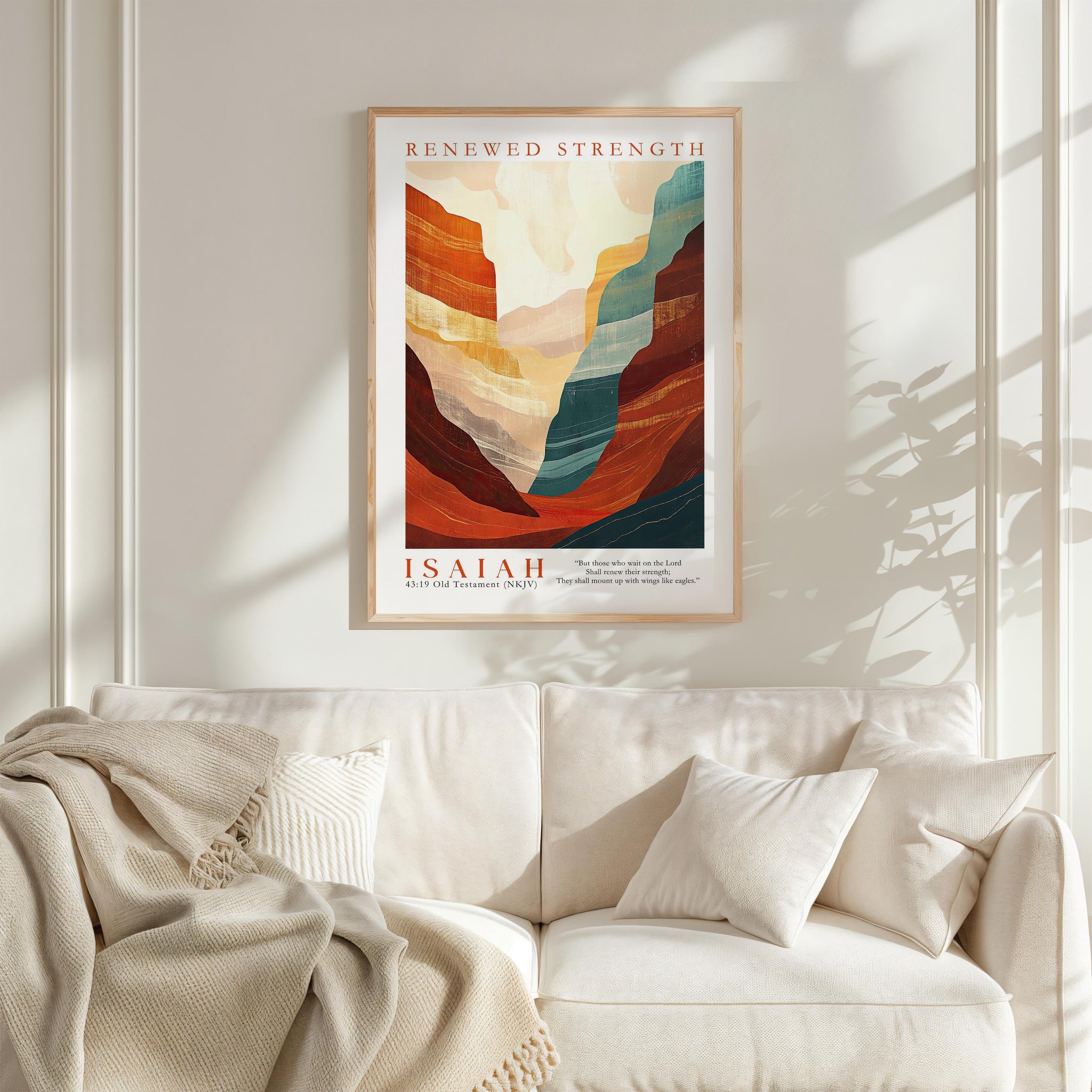 a framed poster of a mountainous landscape with the text "RENEWED STRENGTH" and " Isaiah" below it, hanging on a white wall above a white couch with a blanket draped over it.