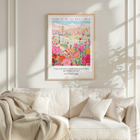 a poster of a cityscape with flowers hanging on a wall above a white couch with pillows.