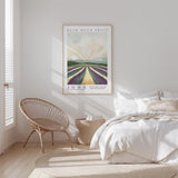 a serene bedroom scene with a bed, a woven chair, and a framed poster of a countryside landscape.