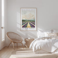 a serene bedroom scene with a bed, a woven chair, and a framed poster of a countryside landscape.