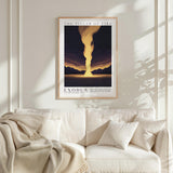 a framed poster of a sunset landscape with a large yellow flame in the center, hanging on a white wall above a white couch with a blanket draped over it.