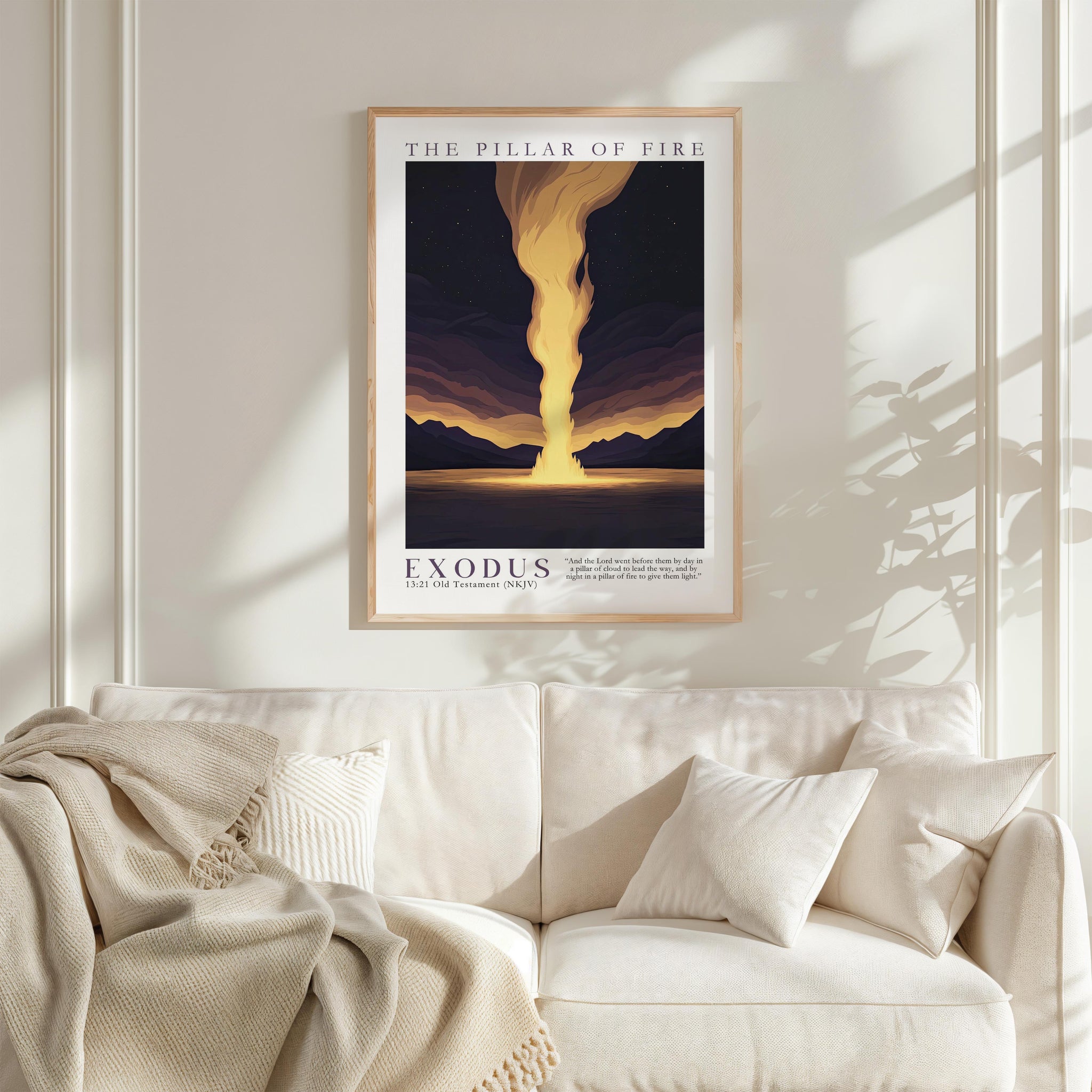 a framed poster of a sunset landscape with a large yellow flame in the center, hanging on a white wall above a white couch with a blanket draped over it.