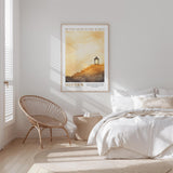 A bedroom with a bed, a woven chair, and a framed poster of a sunset on the wall.