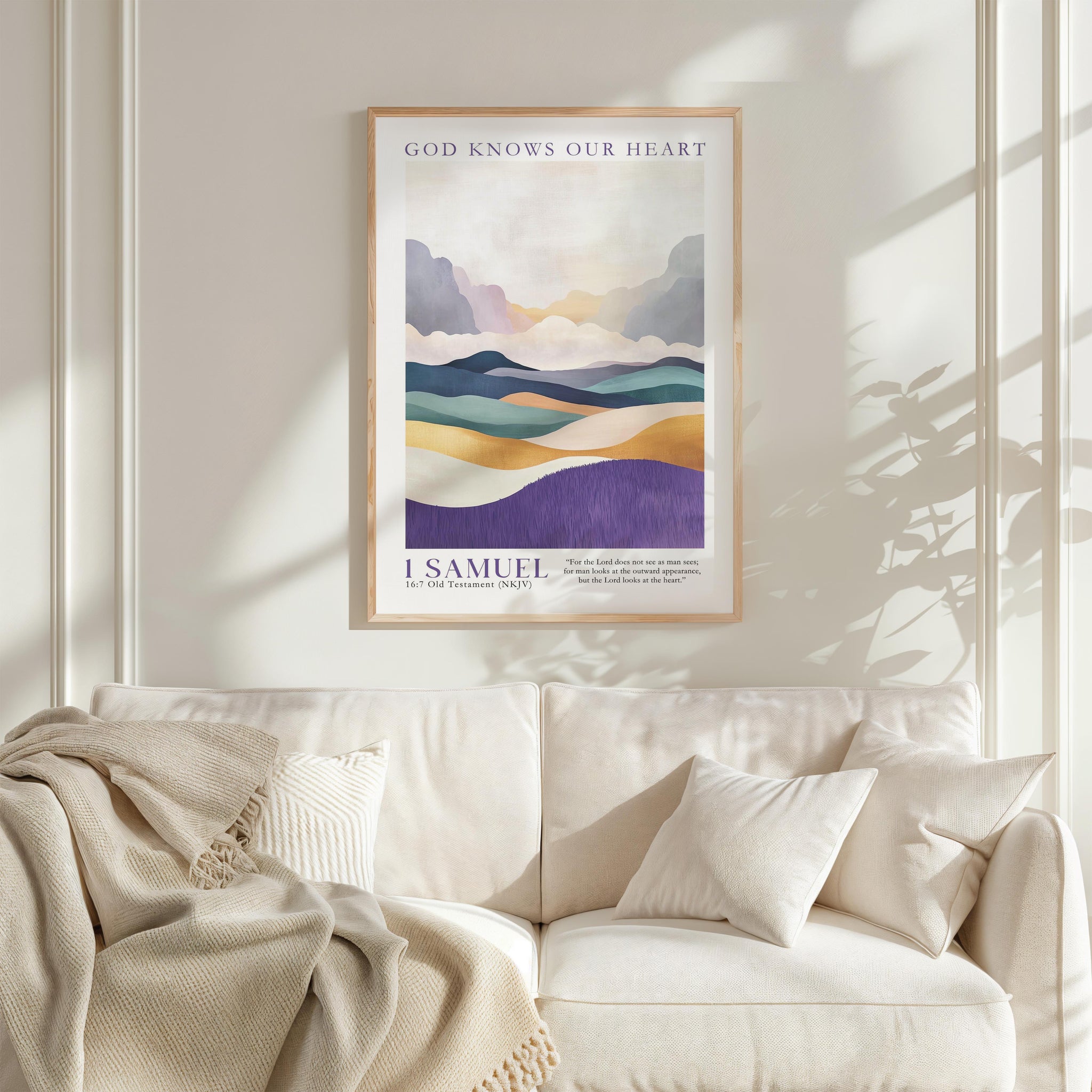 a framed poster of a landscape with mountains and a quote from the Bible, "I Samuel", hanging on a white wall above a white couch with a blanket draped over it.
