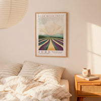 a bedroom setting with a framed poster of a countryside landscape hanging on the wall above a bed with striped bedding.
