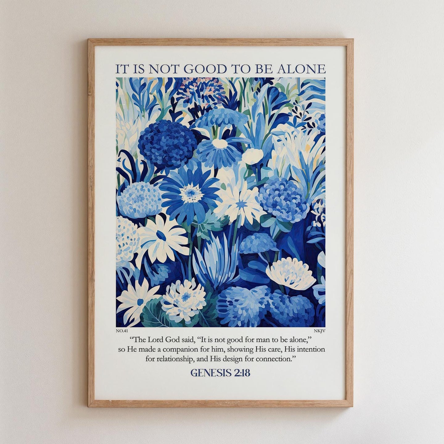 The image is a framed poster with a blue and white floral design. The poster contains a quote from the Bible, specifically Genesis 2:18, which states "It is not good to be alone."