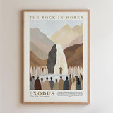 The image is a framed poster depicting a biblical scene from the Old Testament, specifically the story of Exodus. It shows a large rock formation with a waterfall, surrounded by a crowd of people, likely representing the biblical story of the Exodus from Egypt. The poster includes a quote from the Bible, which reads "Behold! I will stand before you on the rock in Horeb, and you shall strike the rock, and water will come out of the rock, and you will drink."