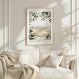 a framed poster of a landscape with greenery hanging on a wall above a white couch with pillows.
