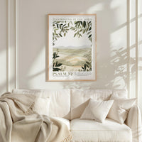 a framed poster of a landscape with greenery hanging on a wall above a white couch with pillows.