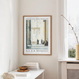 a framed poster of a classical architectural scene, hanging on a wall in a room with a white table and a window.