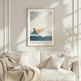 a framed poster of a roll of toilet paper hanging on a wall above a white couch with a blanket draped over it.