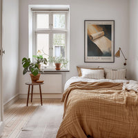 a cozy bedroom with a large bed, a wooden nightstand, and a framed poster on the wall. The room has a warm, inviting atmosphere with a wooden floor and a window with a plant on the sill.