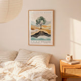 a bedroom scene with a framed poster of a tree and mountains hanging on the wall above a bed with striped bedding.