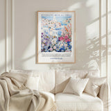 a framed poster of a colorful floral scene hanging on a wall above a white couch with pillows.