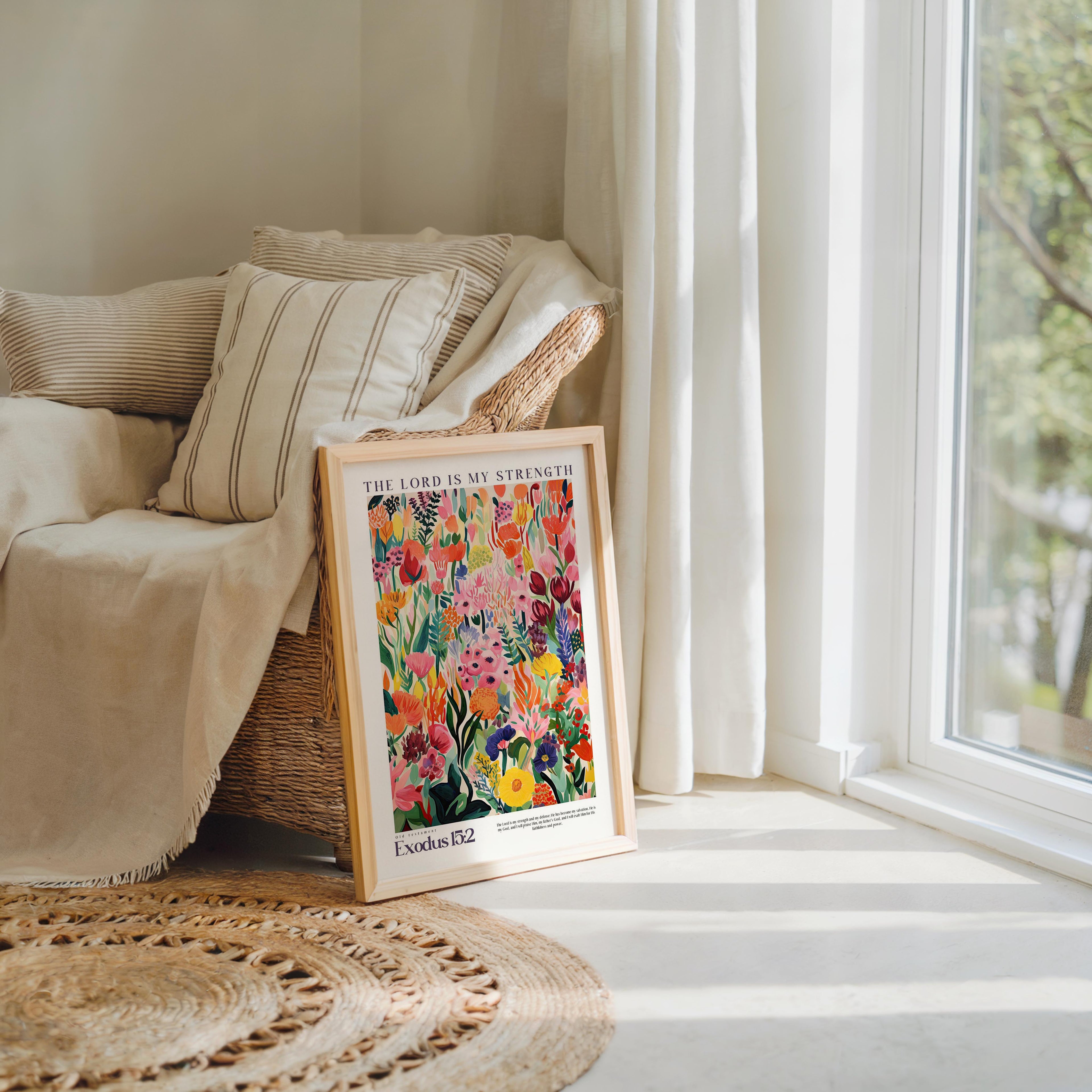 A framed poster of a colorful floral design is propped up against a beige armchair in a sunlit room with a large window.
