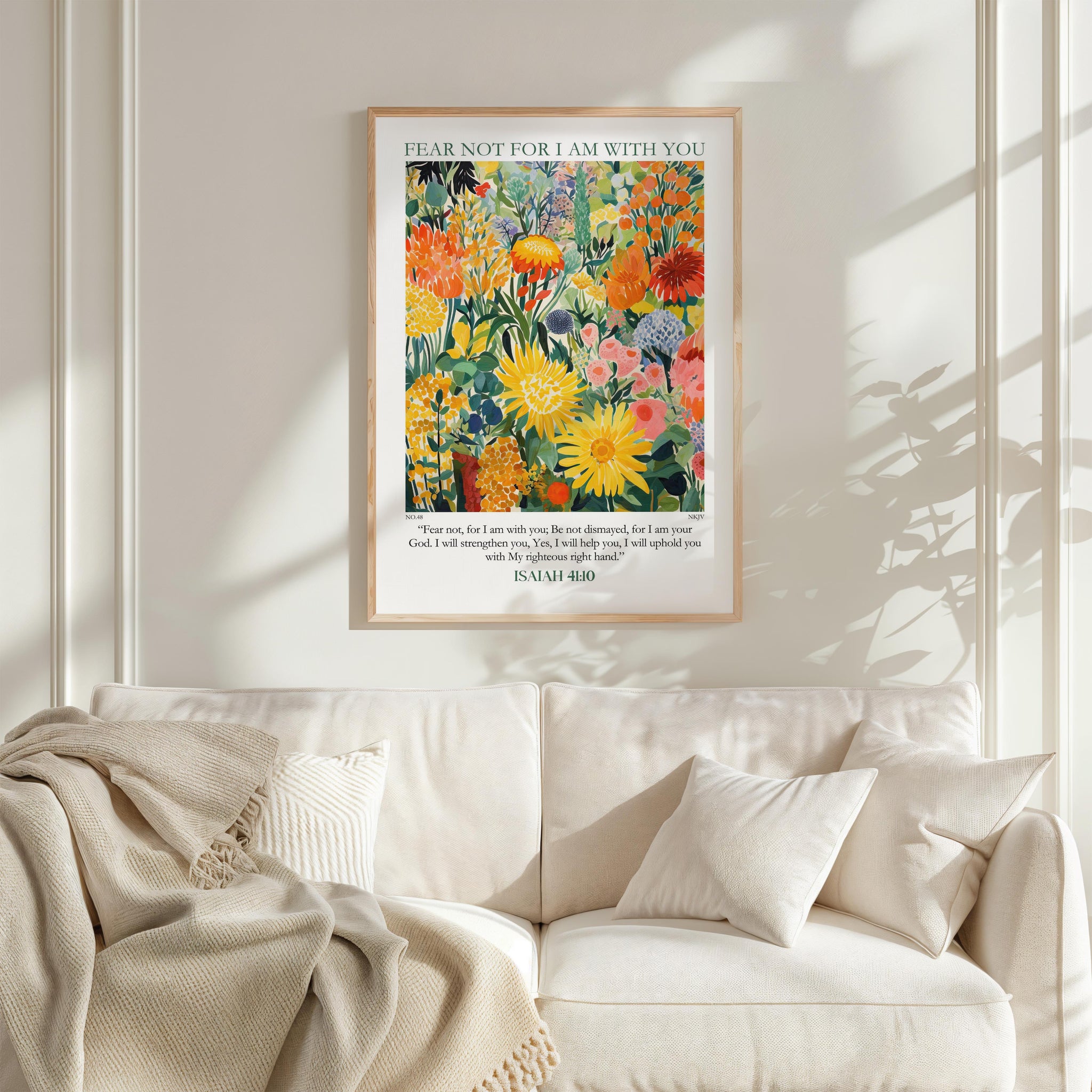 a framed poster of a vibrant floral scene hanging on a white wall above a white couch with a blanket draped over it.
