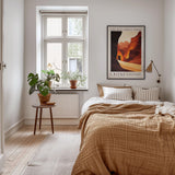 a cozy bedroom with a large bed, a wooden nightstand, and a framed poster on the wall. The room has a warm, inviting atmosphere with a wooden floor and a rug.