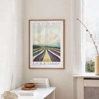 a framed poster of a countryside landscape with a quote about fruit hanging on a wall in a room with a white table and a window.