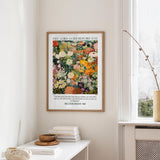 a framed poster of a colorful floral arrangement hanging on a wall, with a window and a small table with books and a bowl in the foreground.