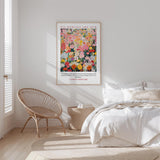 a bedroom with a bed, a woven chair, and a framed poster of a colorful floral design on the wall.