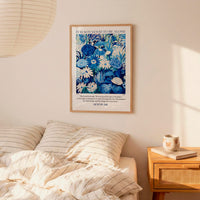 a bedroom setting with a framed poster of a blue floral pattern hanging on the wall above a bed with striped pillows.