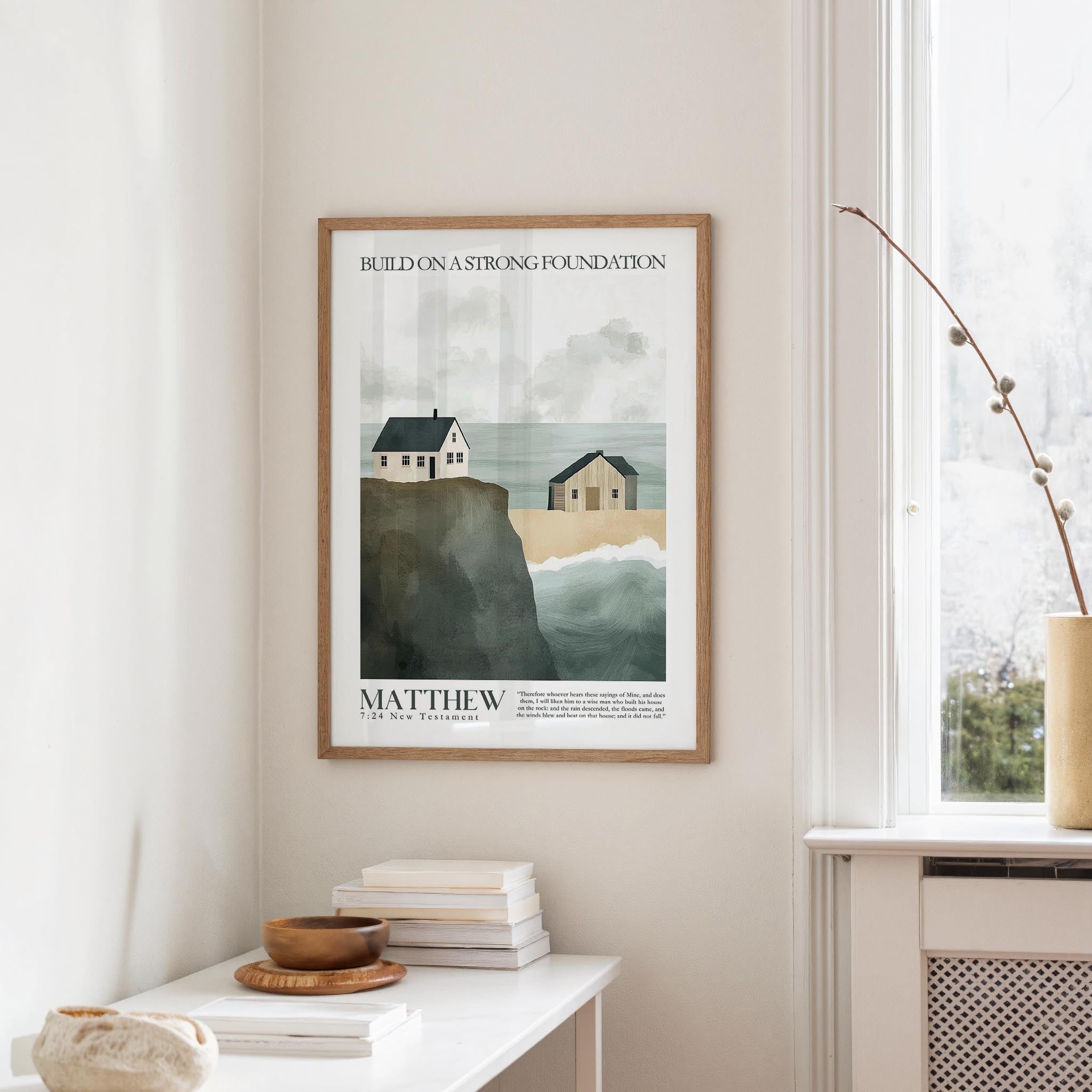 a framed poster of a coastal scene with houses and cliffs, hanging on a wall in a room with a white table and a window.