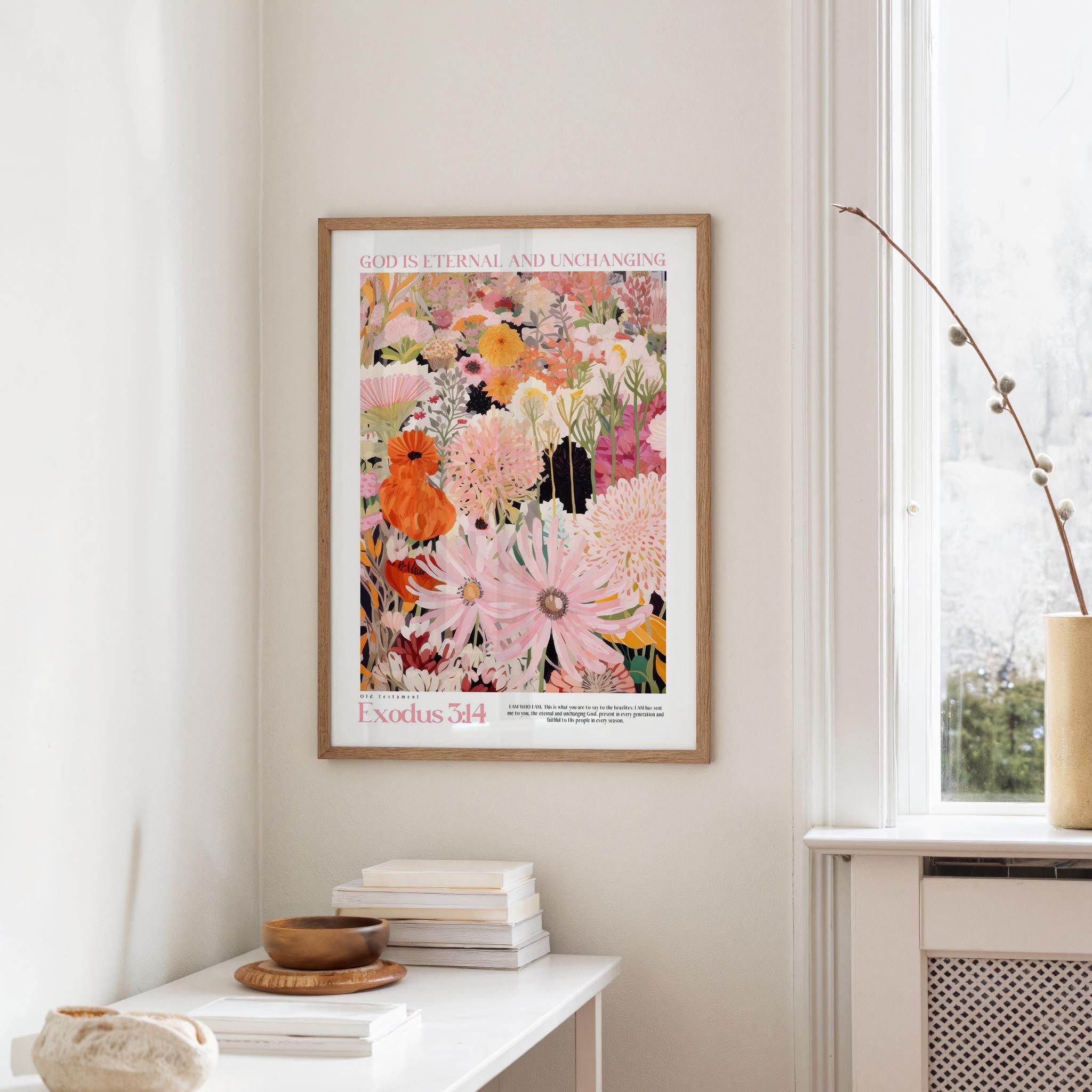 a framed poster of a colorful floral design hanging on a wall, with a white table and a vase of flowers in the foreground.