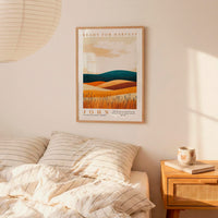 a bedroom scene with a framed poster of a landscape hanging on the wall above a bed with striped pillows.
