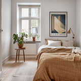 A cozy bedroom with a large bed, a nightstand, and a potted plant. The room has a warm, inviting atmosphere with a wooden floor and a window with a view of trees outside.