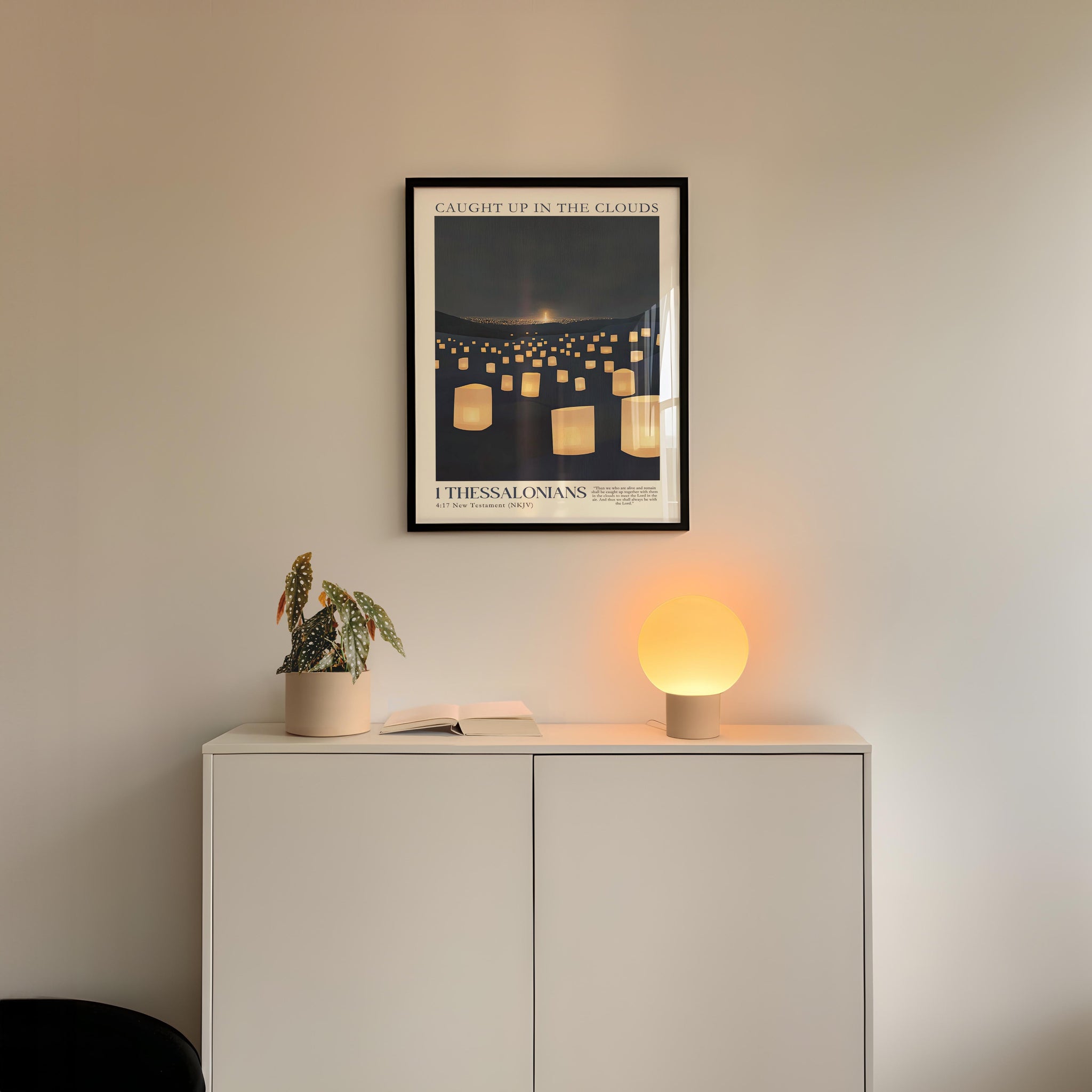 a white cabinet with a potted plant and a lamp on top, set against a white wall. Above the cabinet, there is a framed poster with a black border and white text.