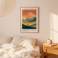 a bedroom scene with a framed poster of a mountain landscape hanging on the wall above a bed with striped bedding.