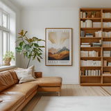 a cozy living room with a large bookshelf filled with books, a comfortable leather sofa, and a framed poster of a landscape on the wall.