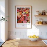 A framed poster of a vibrant floral arrangement hangs on a white wall above a wooden countertop, which has a bowl of lemons and a plant on it.