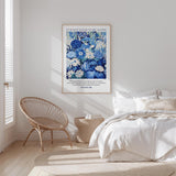 a serene bedroom scene with a bed, a woven chair, and a framed poster of blue flowers on the wall.