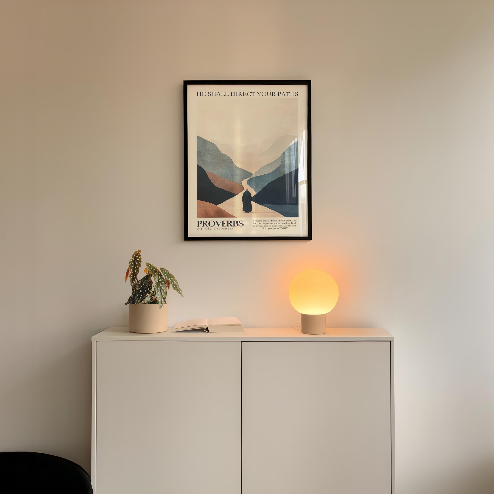 a minimalist interior design with a framed poster of a mountain landscape above a white cabinet with a plant and a lamp on top.