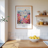 a kitchen scene with a framed poster of a colorful garden hanging on the wall above a wooden countertop with a bowl of lemons.