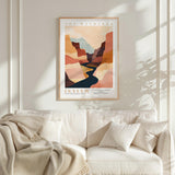 a framed poster of a desert landscape with a winding river, hanging on a wall above a white couch with a blanket draped over it.