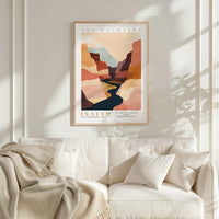 a framed poster of a desert landscape with a winding river, hanging on a wall above a white couch with a blanket draped over it.