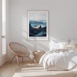 a serene bedroom scene with a bed, a woven chair, and a framed poster of a mountain landscape.