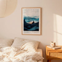 a bedroom scene with a framed poster of a mountain landscape hanging on the wall above a bed with striped bedding.