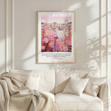 a framed poster of a cityscape with pink flowers hanging on a wall above a white couch with a blanket draped over it.