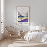 A bedroom with a bed, a woven chair, and a framed poster of a landscape on the wall.