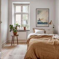 a cozy bedroom with a large bed, a wooden nightstand, and a window with a plant on the sill. The room has a warm, inviting atmosphere with a neutral color palette and natural elements like the potted plant.