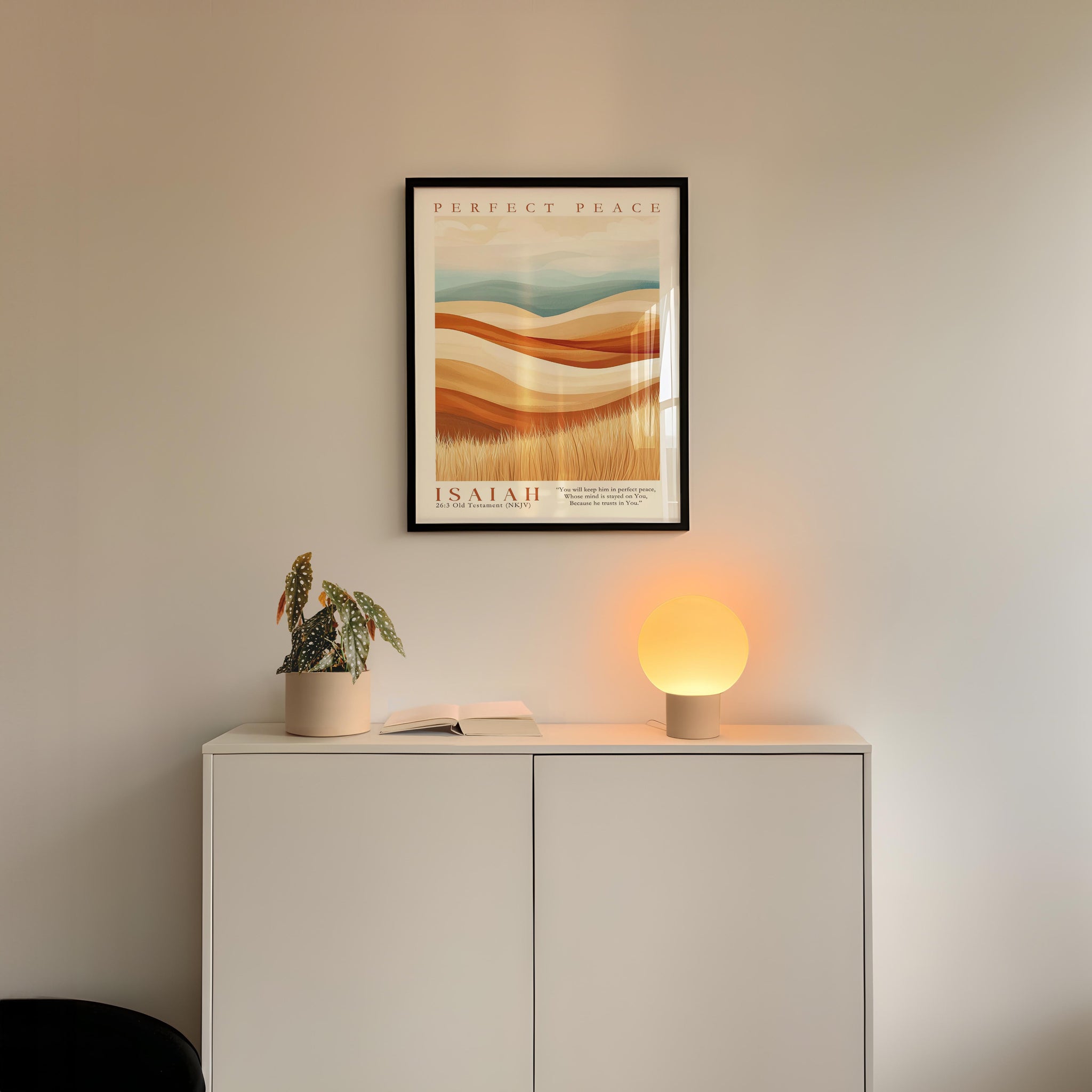 a minimalist interior design with a framed poster of a desert landscape above a white cabinet with a plant and a lamp on top.
