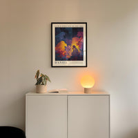 a white cabinet with a plant and a lamp on top, and a framed poster hanging on the wall above the cabinet.