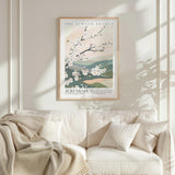 a framed poster of a floral design hanging on a wall above a white sofa with a blanket draped over it.