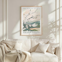 a framed poster of a floral design hanging on a wall above a white sofa with a blanket draped over it.
