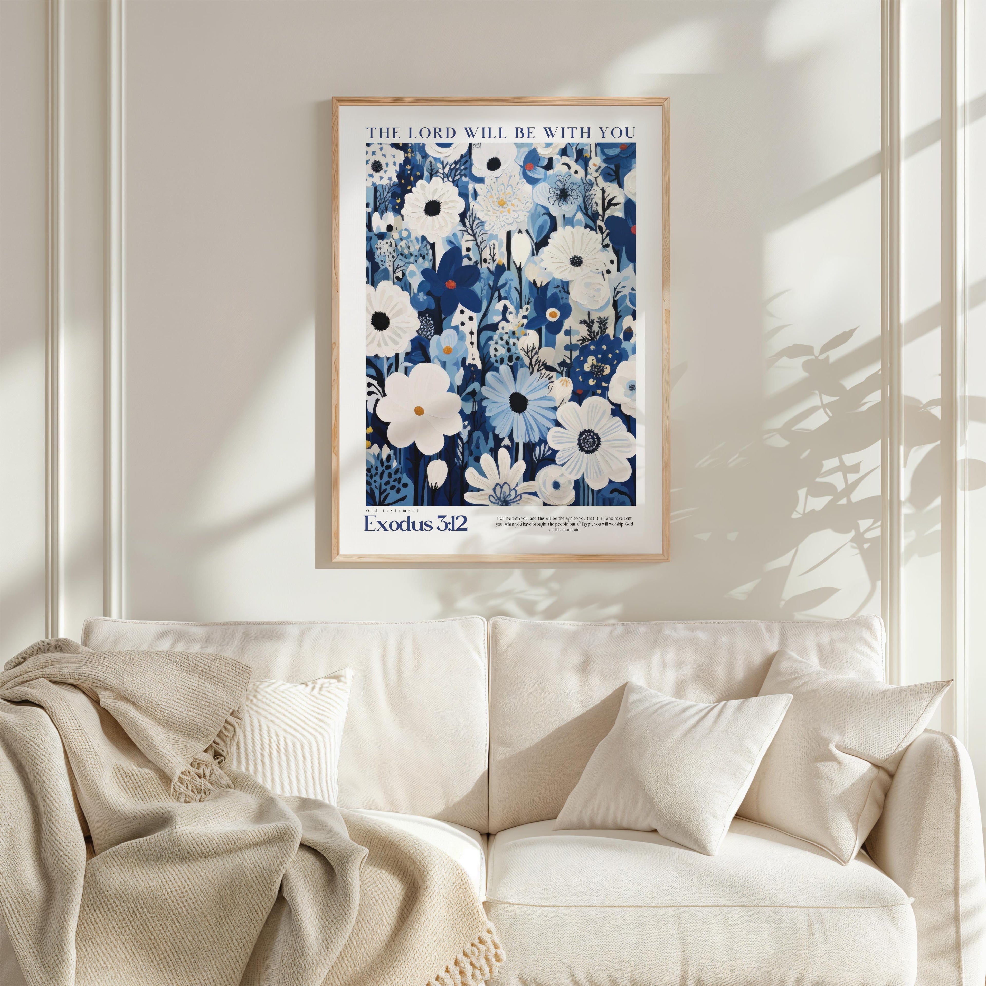 a framed poster of a floral design hanging on a white wall above a white couch with a blanket draped over it.