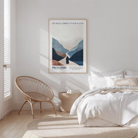 a serene bedroom scene with a bed, a woven chair, and a framed poster of mountains on the wall.